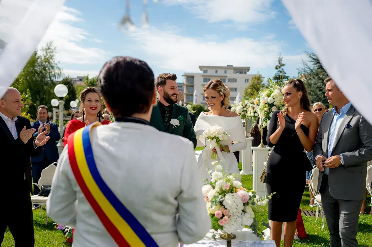 Ceremonia civilă în aer liber, invitații aplaudând în jurul mirilor