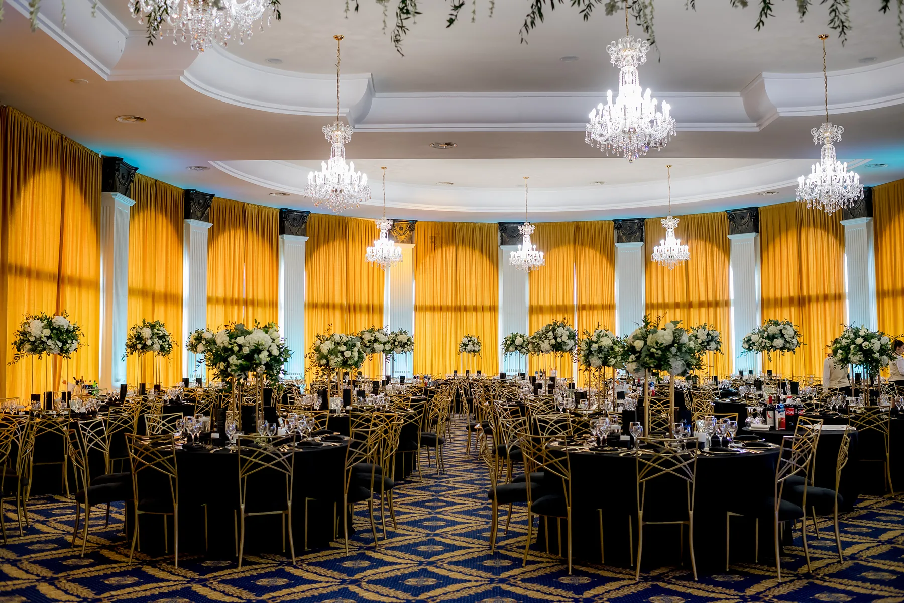 Sală de recepție cu candelabre, draperii aurii și mese decorate, pregătită pentru nuntă în Cluj