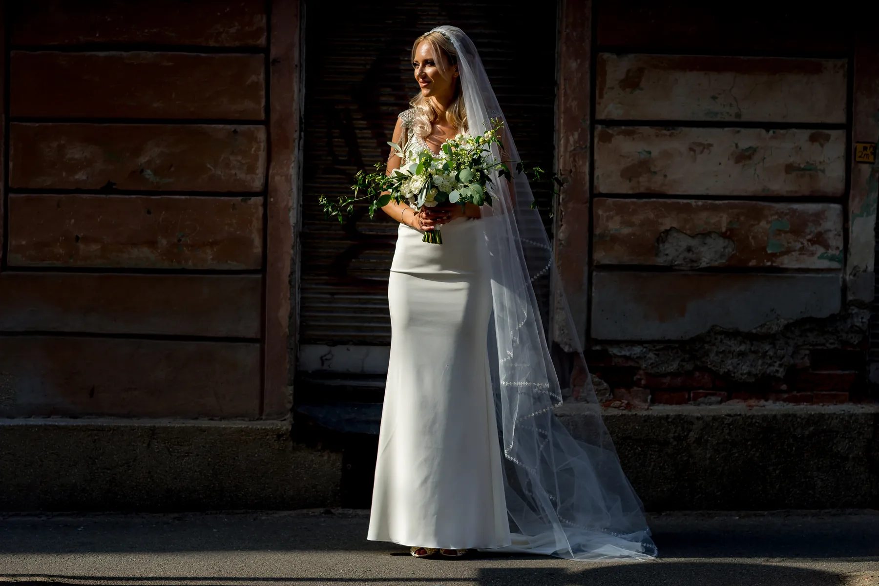 Mireasa în rochie cu voal lung — portret elegant lângă un zid patinat