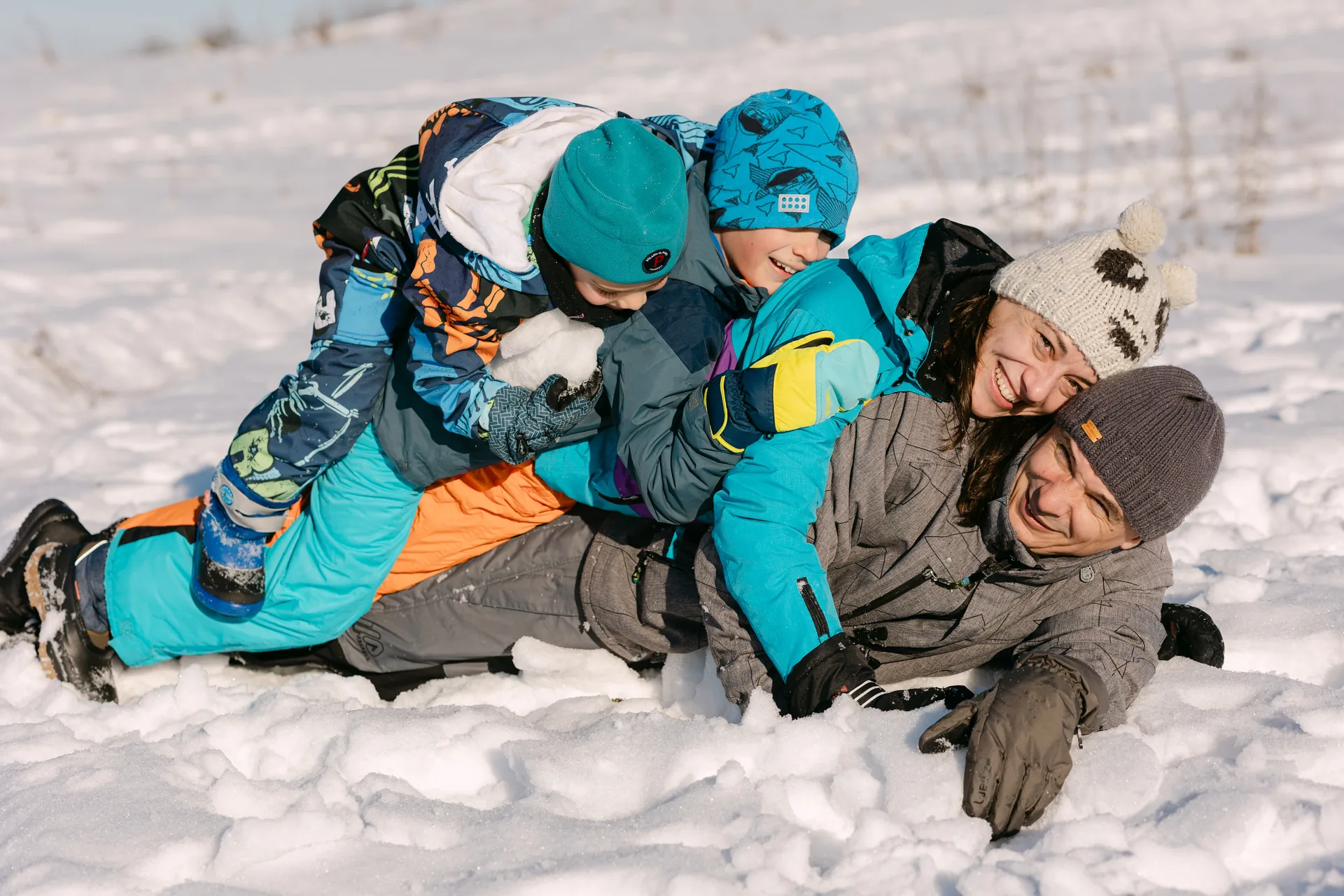 Grămadă de familie tăvălindu-se împreună în zăpadă, râzând cu toții