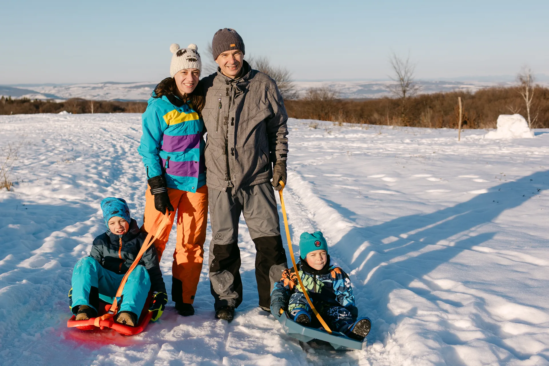 Portret de familie în zăpadă: părinții în picioare, copiii pe sănii