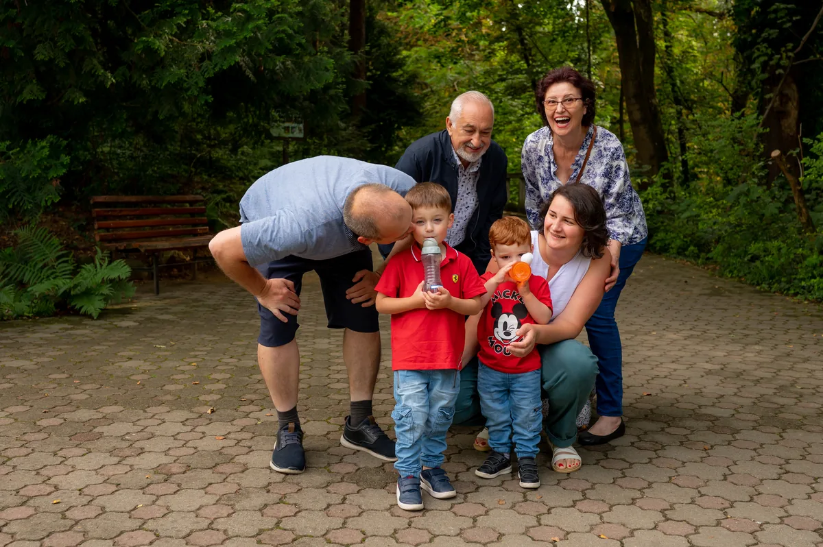 Trei generații râzând împreună la ședință foto de familie — bunici, părinți și doi copii, în Grădina Botanică din Cluj-Napoca