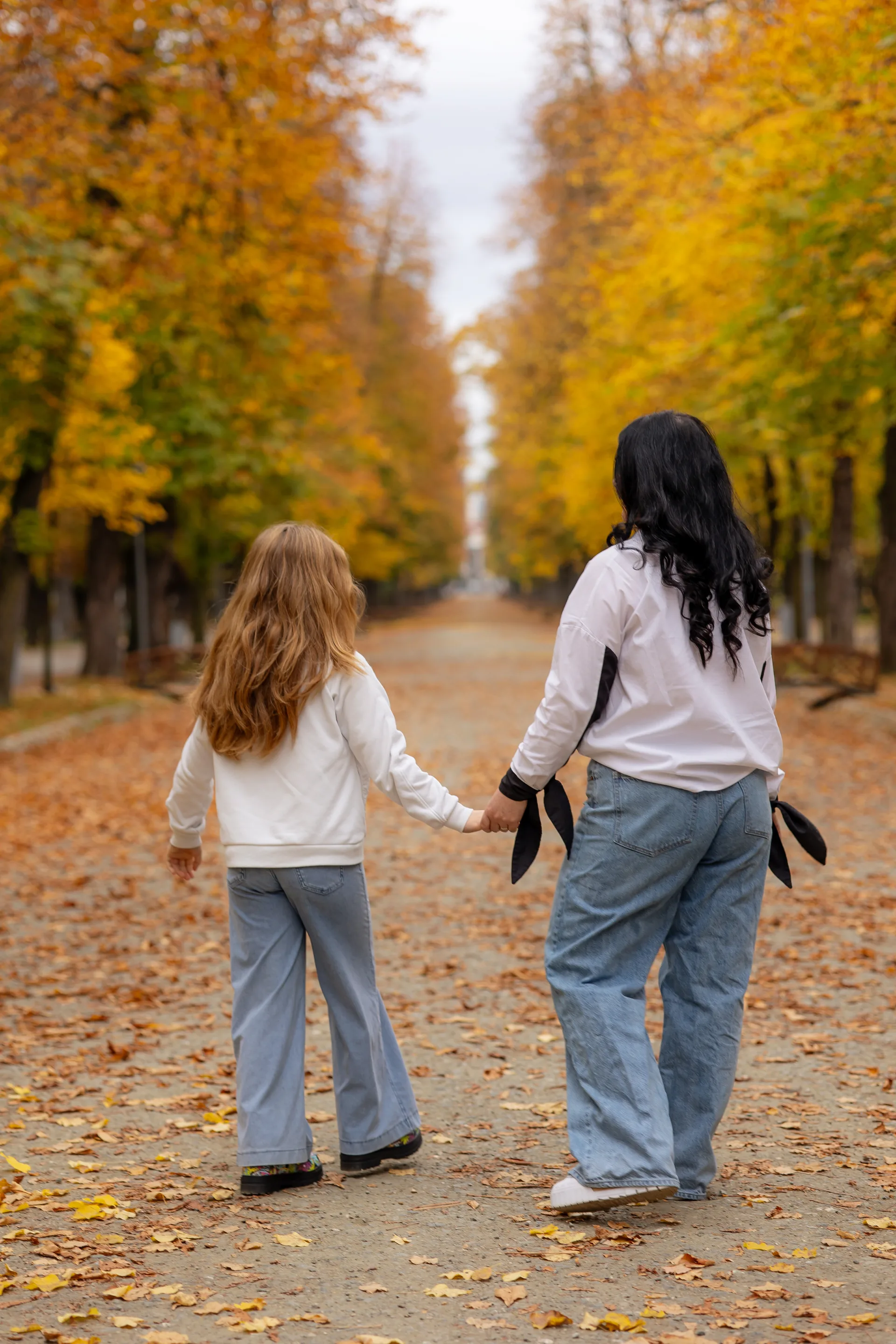 Din spate: mama și fiica mergând pe aleea de arțari din Parcul Central
