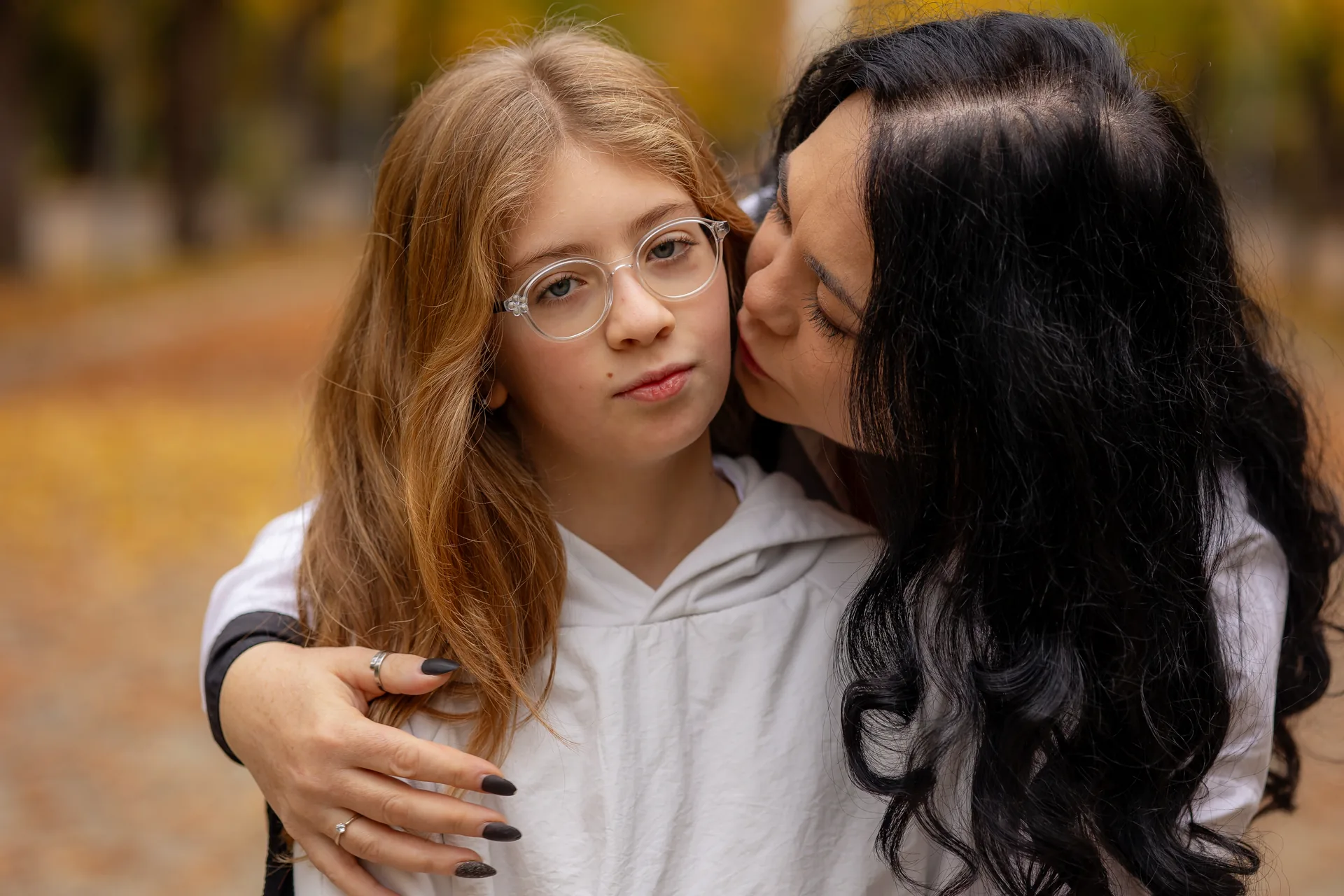 Mama sărutând obrazul fiicei, prim-plan pe fundal de frunze