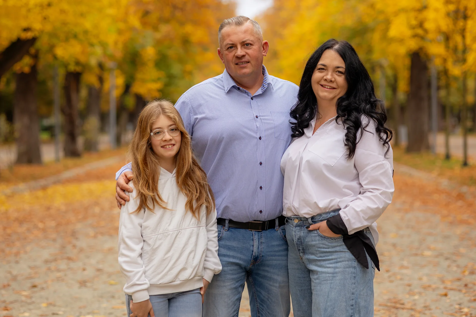 Familia întreagă, părinții și fiica, pe aleea de toamnă