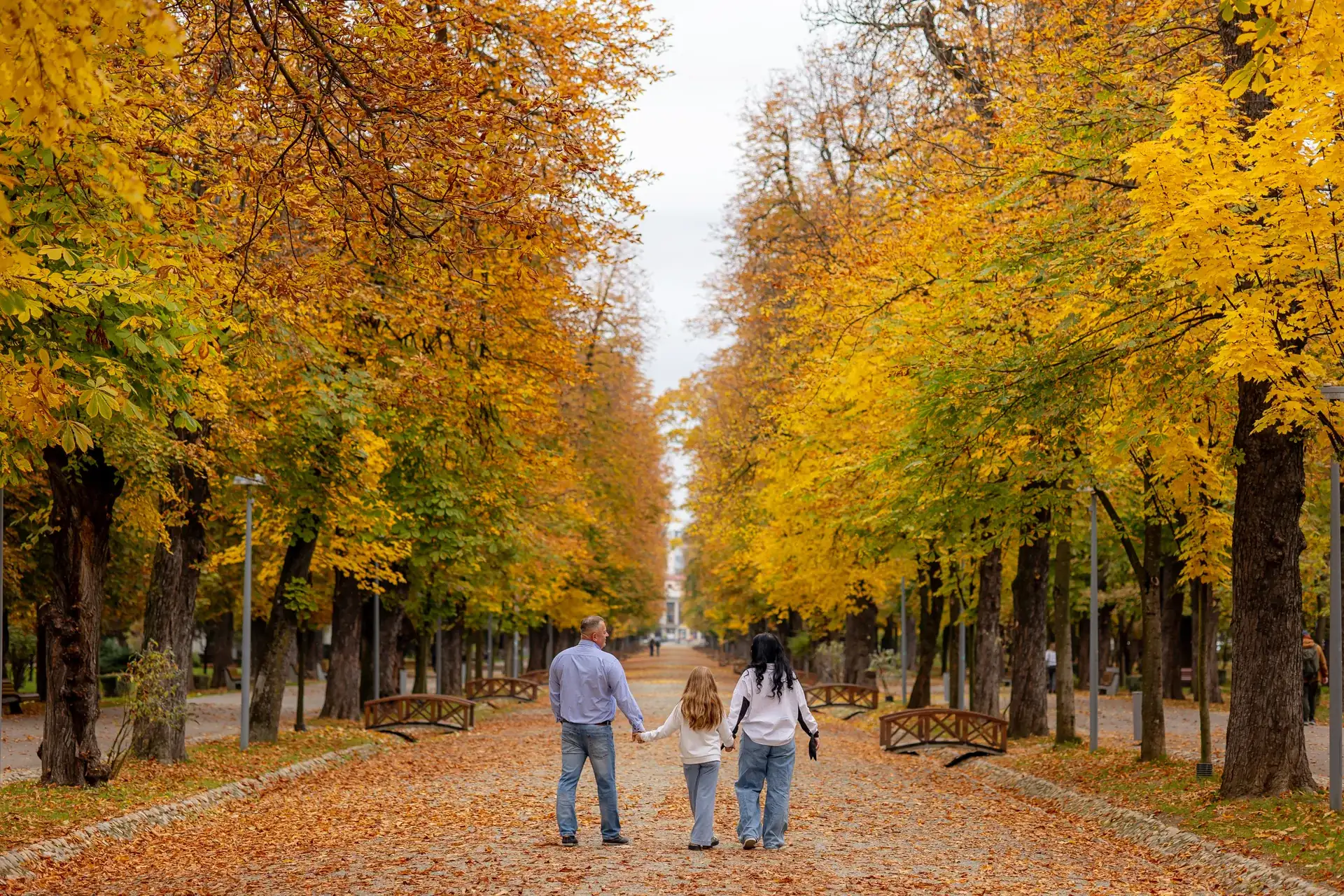Cadru larg: cei trei mici pe aleea lungă din Parcul Central, sub coroanele galbene