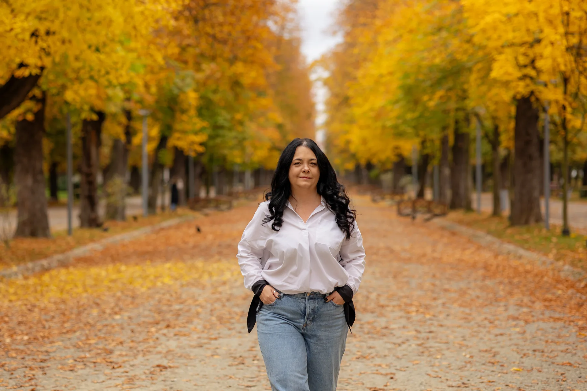 Mama în picioare pe alee, cu brațele desfăcute, zâmbind