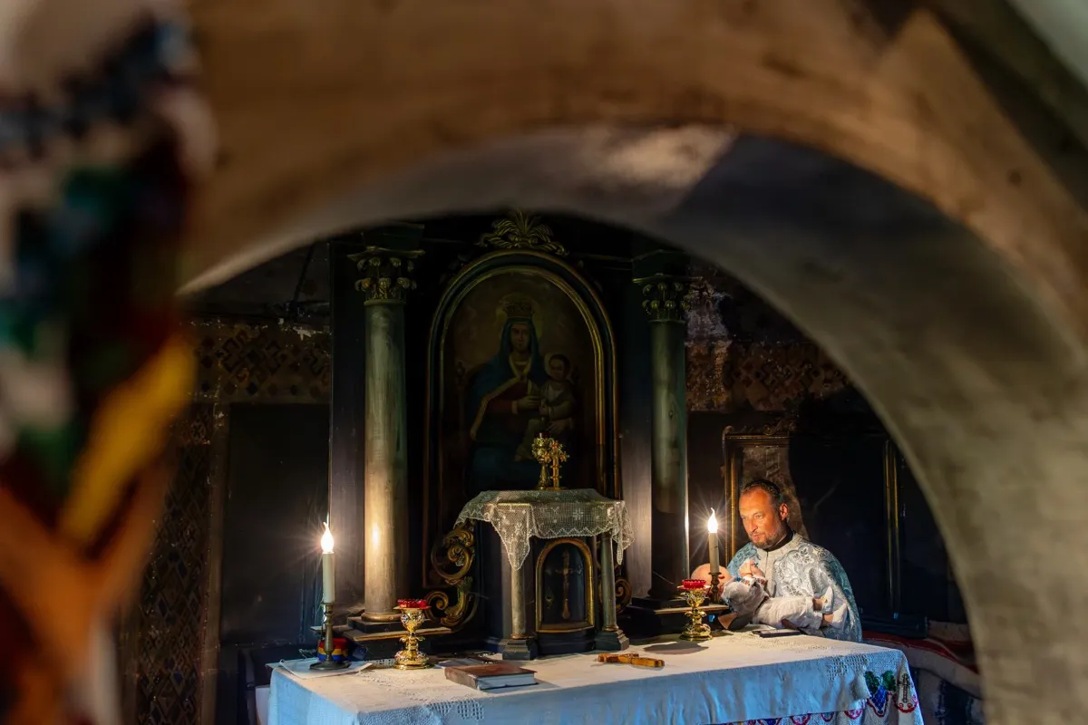 Preot ținând copilul la altar, în lumina lumânărilor, într-o biserică tradițională din Maramureș