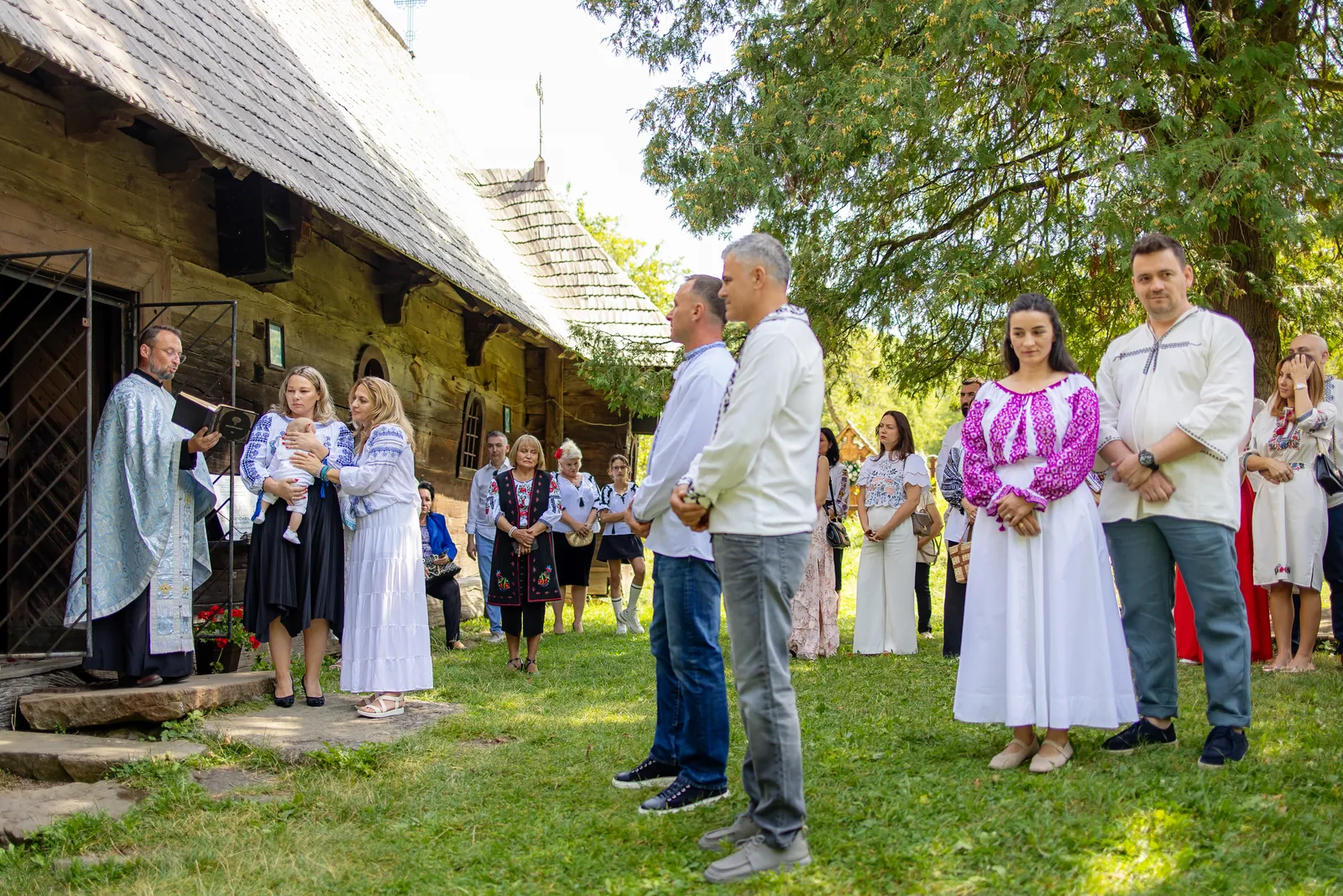Preotul citind în fața bisericii de lemn Sfinții Arhangheli din Breb, invitații pe prag