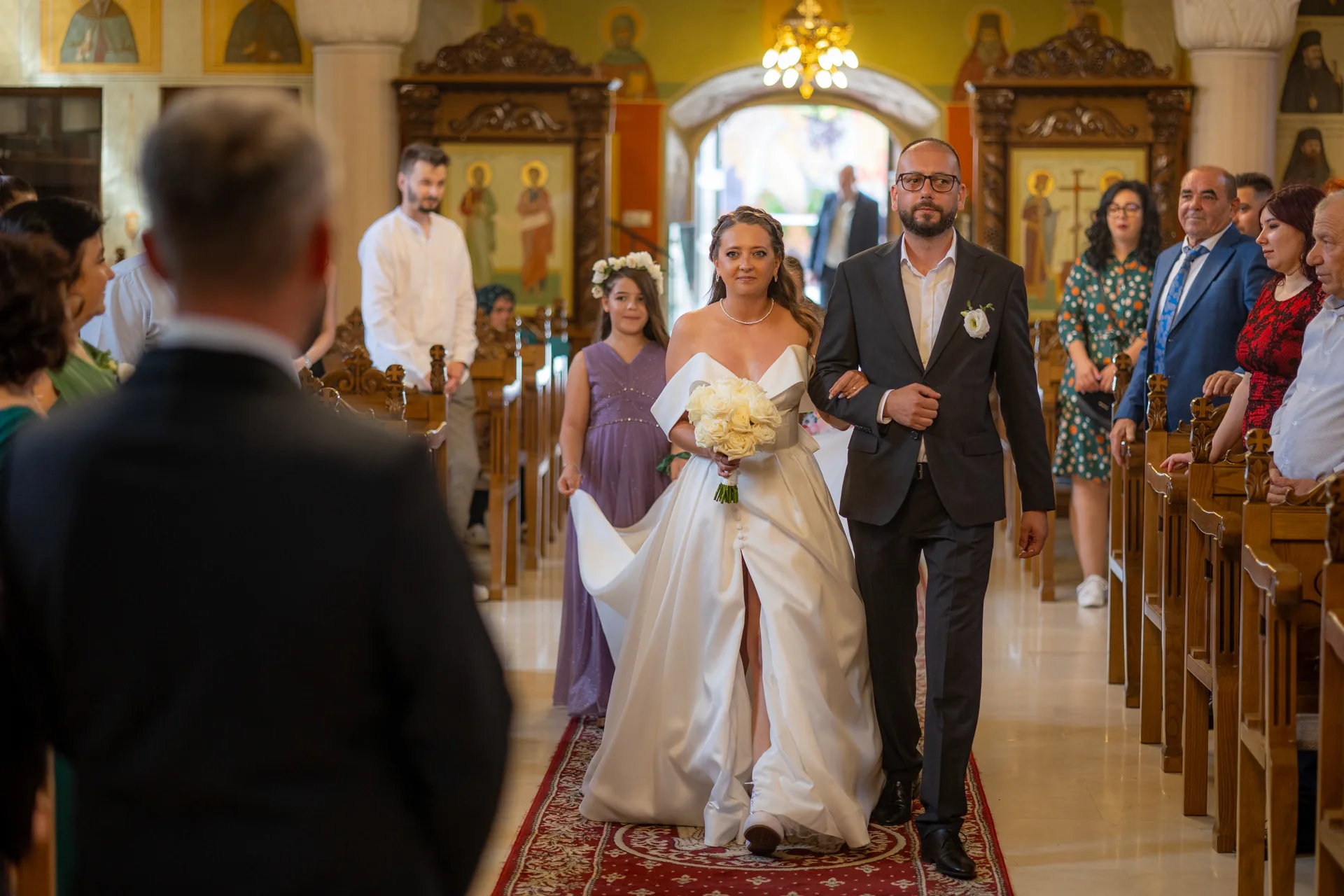 mireasa intră în biserică la braț, pe covorul roșu, între băncile de lemn