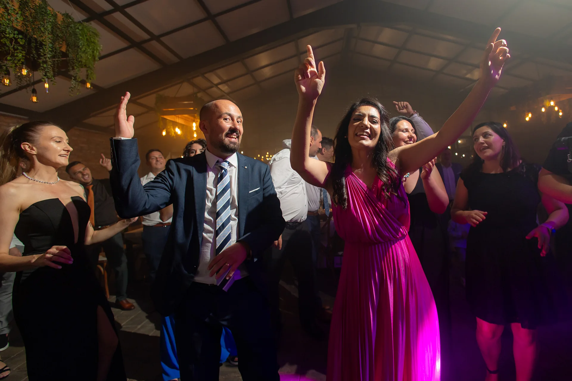 invitați dansând cu mâinile sus, în lumina roz a petrecerii