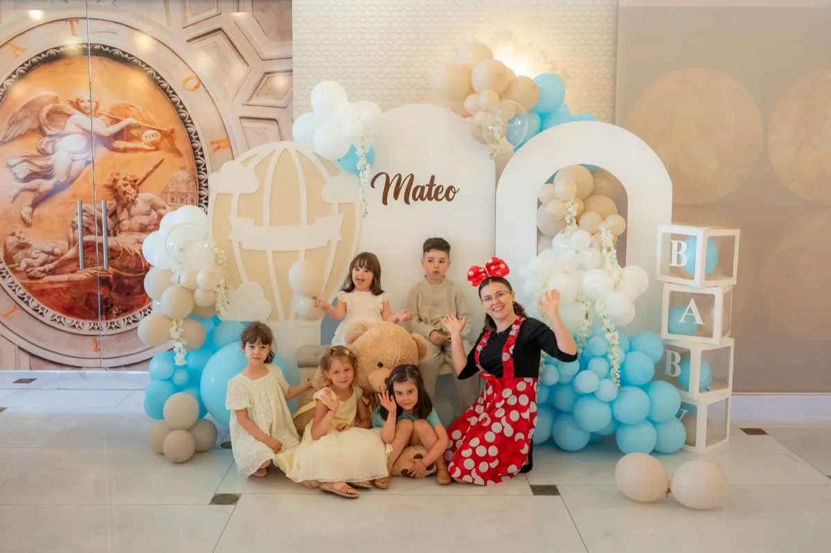 Animatoare costumată alături de copii la photocorner-ul de botez, cu baloane și arcadă decorativă
