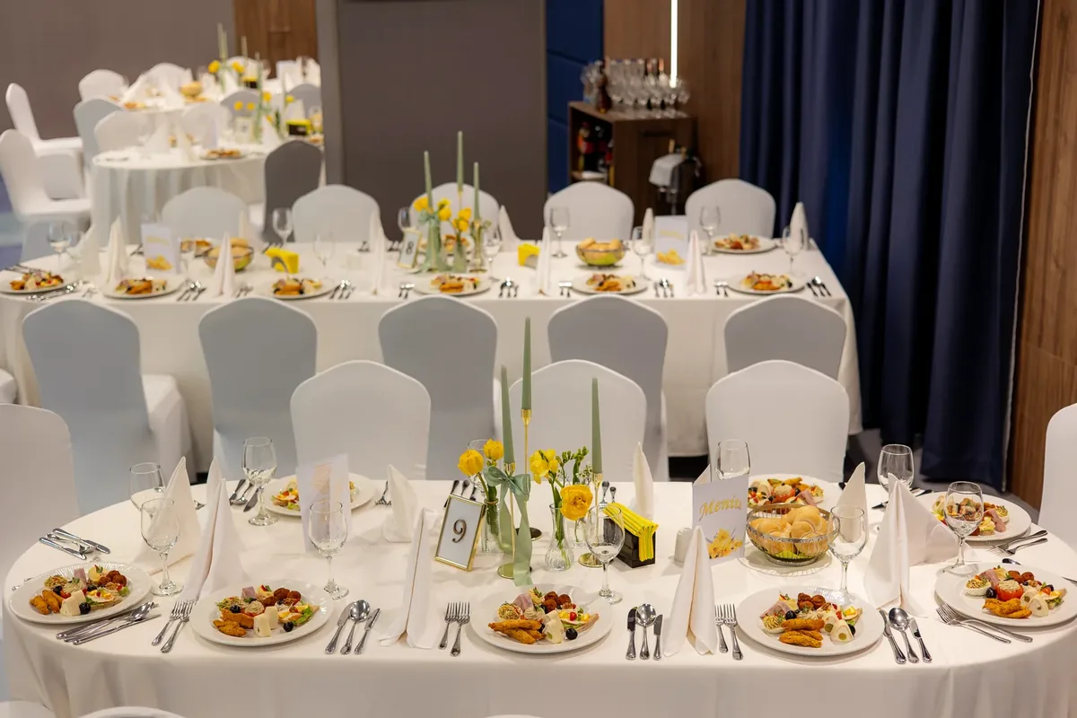 Sală de botez aranjată elegant la un hotel din Cluj-Napoca — mese rotunde cu fețe albe, aperitive și aranjamente florale galbene