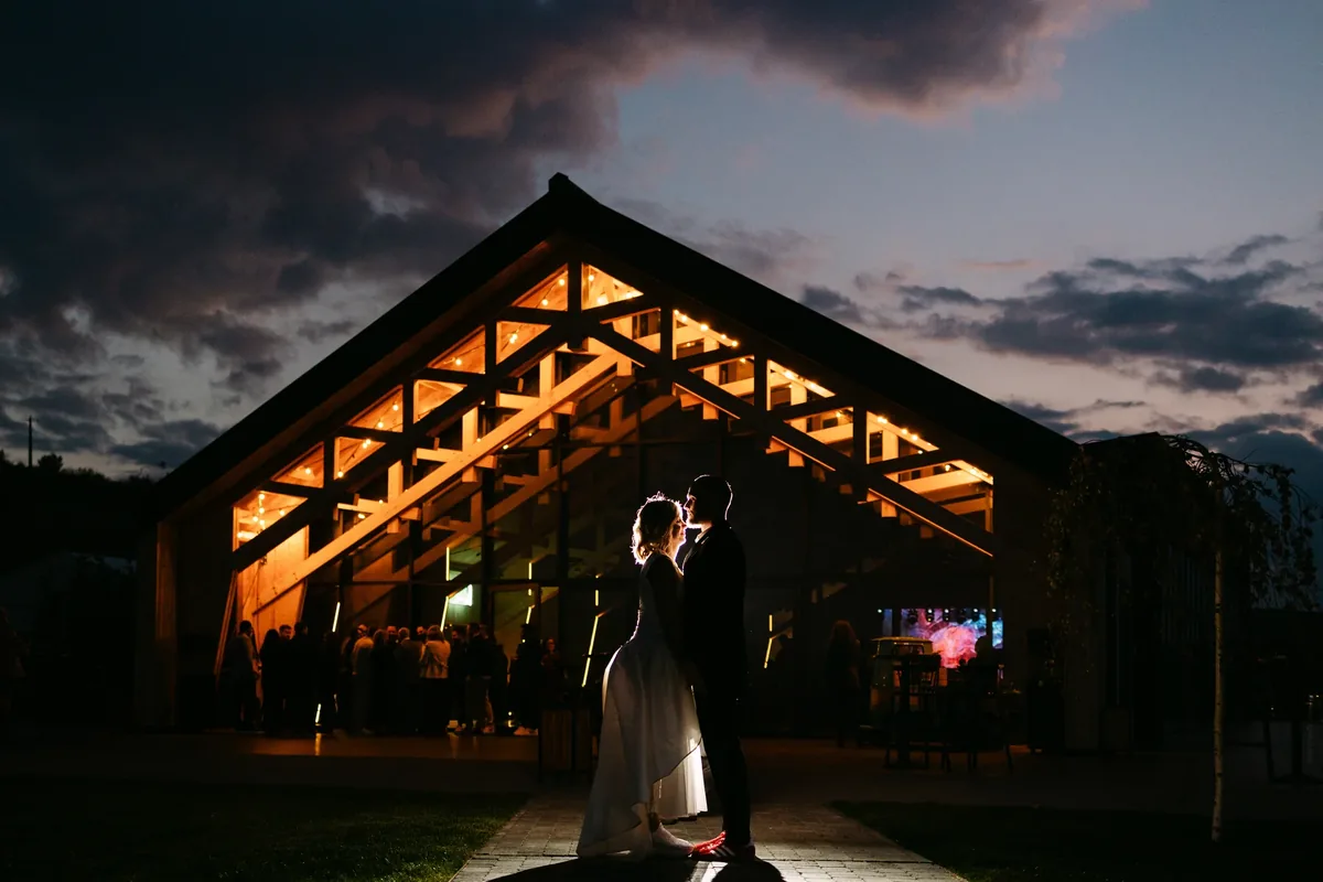 silueta locației The Barn iluminate noaptea, cu mirii în prim-plan