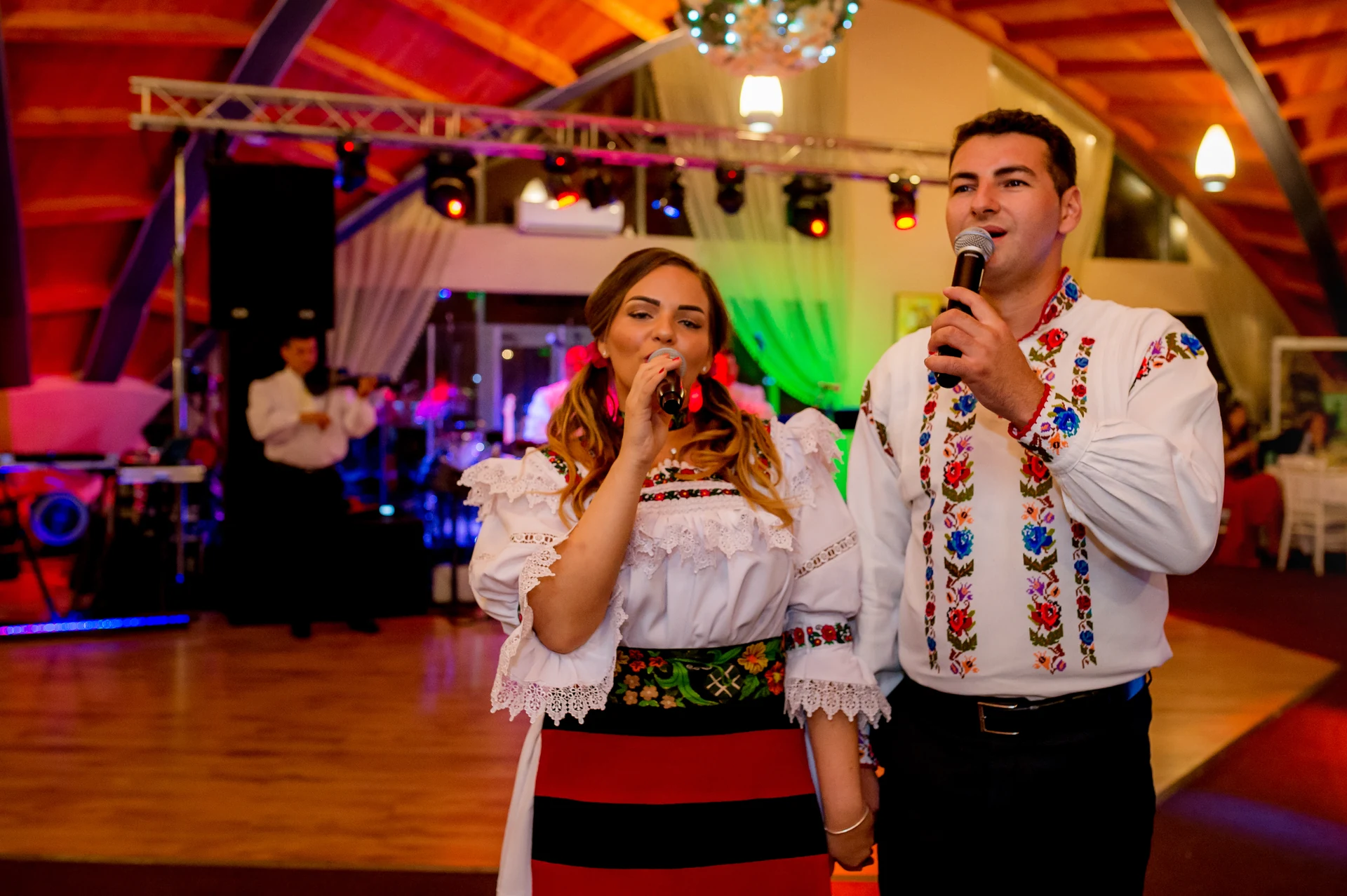 Doi soliști în port maramureșean, ie cu volane și cămașă brodată, cântând la petrecerea de nuntă